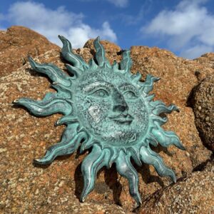 Bronze verdigris sun face wall sculpture displayed on Guernsey granite rocks by the sea