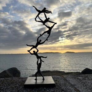 Abstract acrobatic balance bronze sculpture silhouetted against a sunrise over the sea