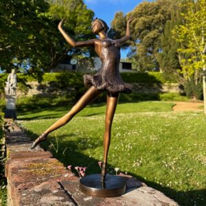 Bronze ballerina sculpture dancing gracefully in a summer garden setting