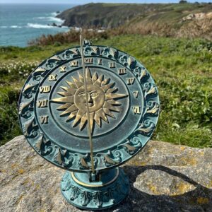 Bronze armillary sphere sundial with sun face dial on Guernsey coastal cliffs overlooking the sea