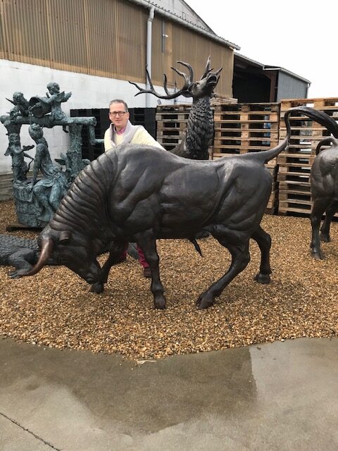 Life size bronze charging bull sculpture with artist standing beside it at outdoor showroom display