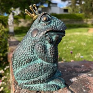 Regal Frog Prince bronze sculpture with golden crown in a garden setting