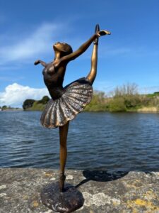 Bronze ballerina sculpture with leg raised in elegant ballet pose by water