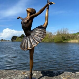 Bronze ballerina sculpture with leg raised in elegant ballet pose by water