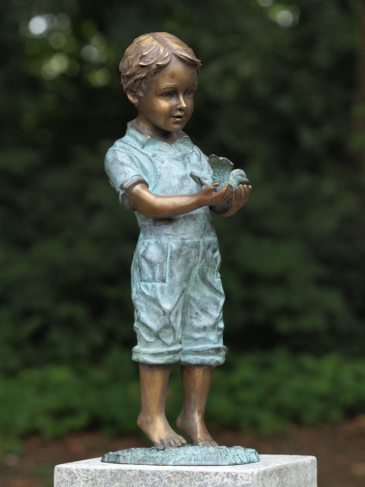 Bronze boy holding bird garden sculpture with verdigris outfit and compact figurative design