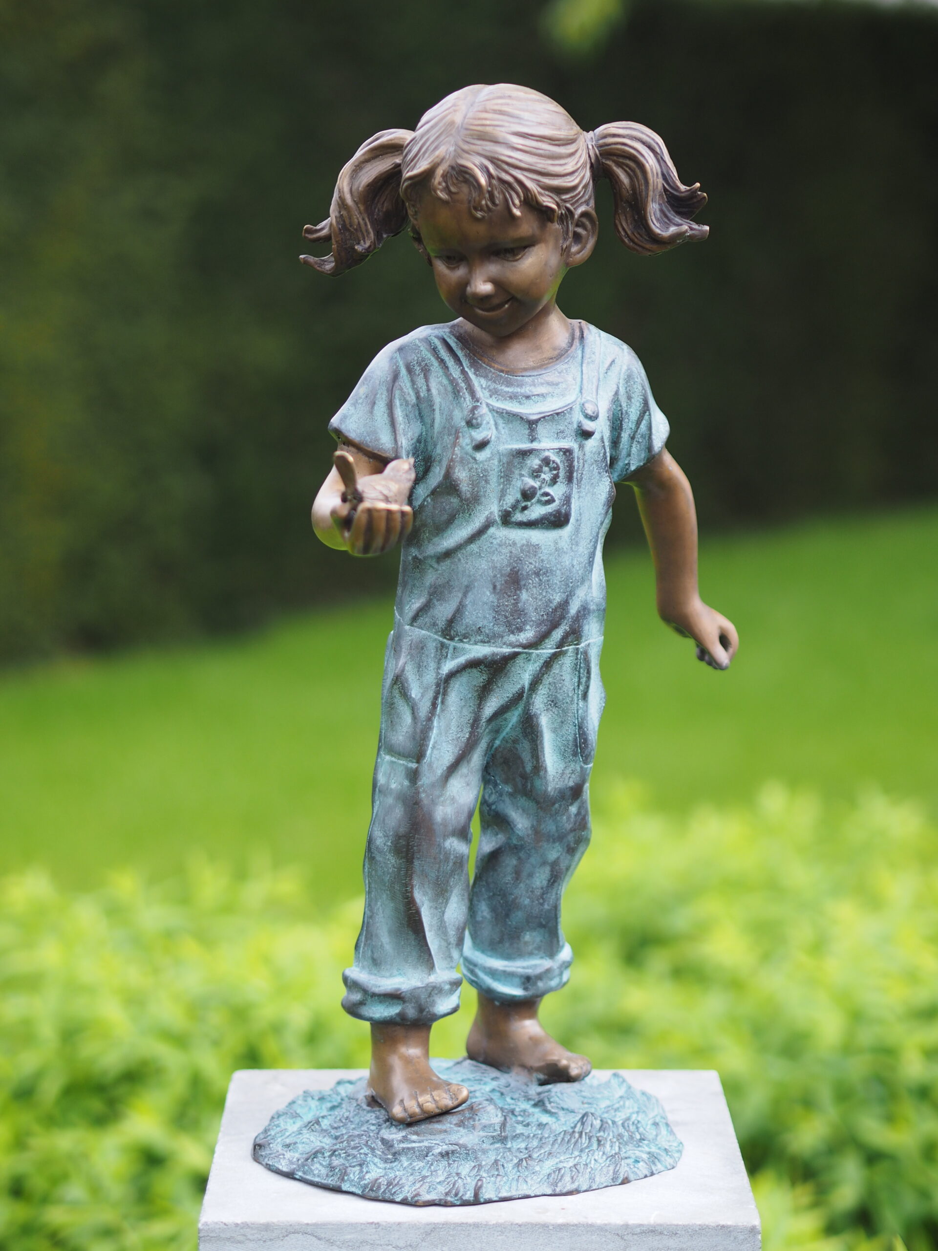 Bronze young girl holding bird sculpture with verdigris dungarees and playful figurative detail