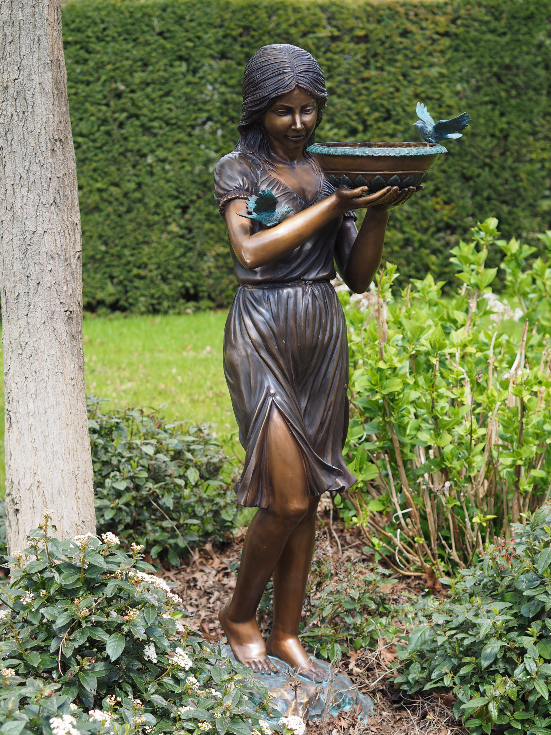 Bronze fountain sculpture of woman holding bowl with birds in classical garden setting