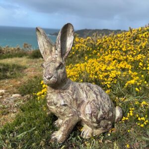 Bronze French rabbit garden sculpture with aged patina set in coastal wild flowers over looking the sea
