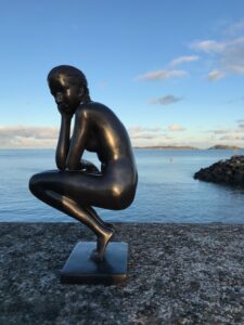 Contemporary bronze nude woman sculpture beside Guernsey harbour at sunset