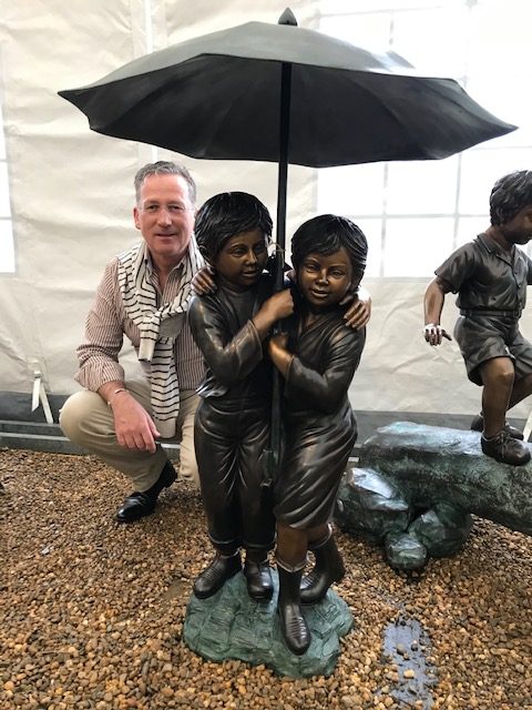 Bronze boy and girl under umbrella garden fountain sculpture with water flowing into pond creating a charming family garden feature