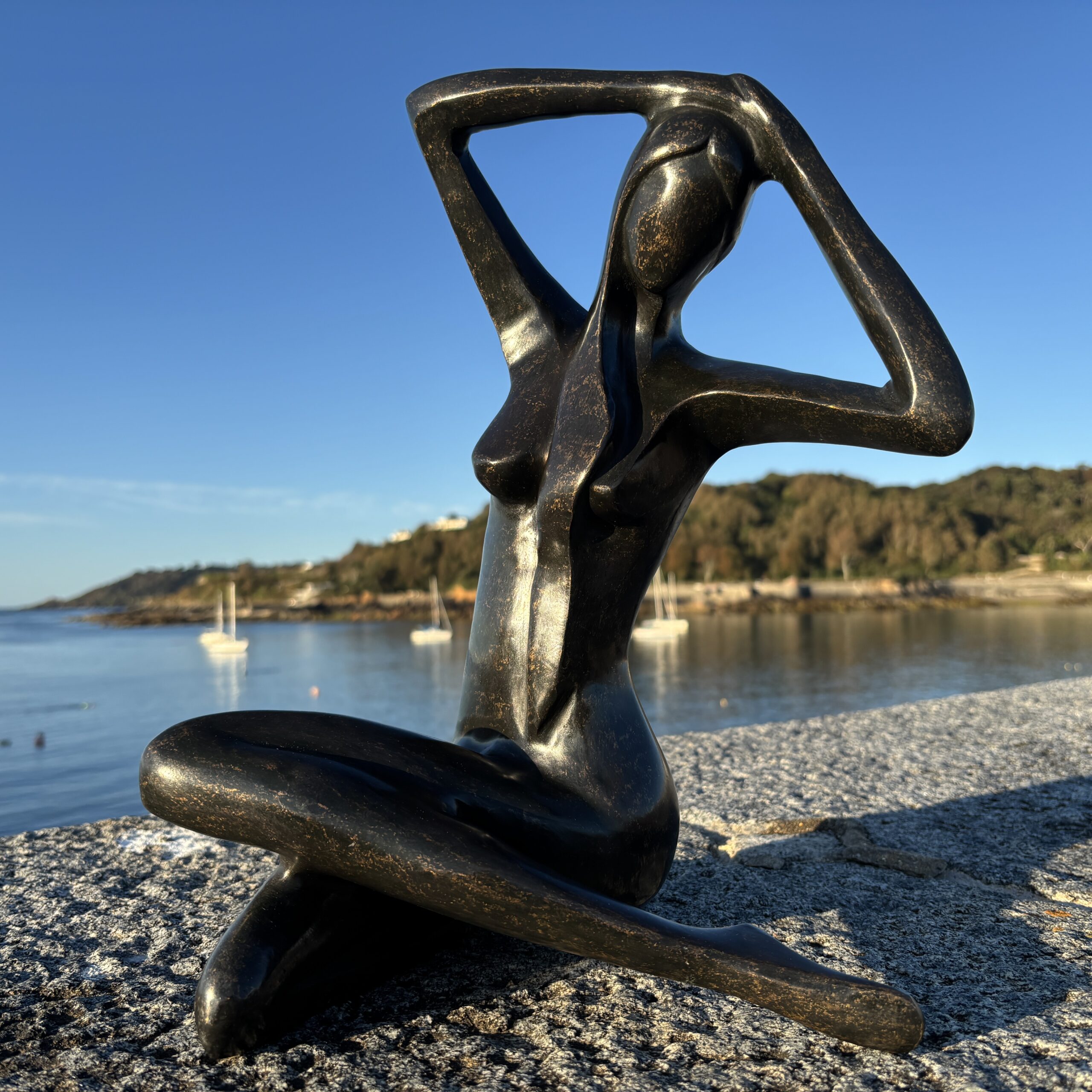 Abstract Female Nude Bronze Sculpture – Modern Seated Woman Figure front view with elegant raised arms beside the Guernsey coast