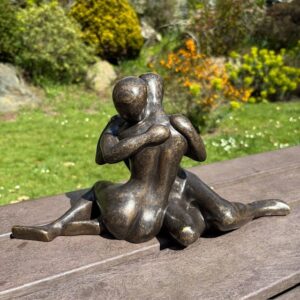 Modern bronze couple sculpture showing a quiet intimate embrace in a garden setting