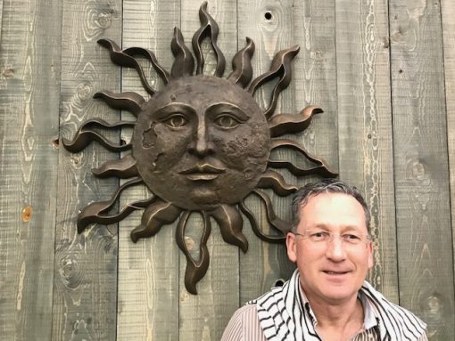 Solid bronze sunface wall art sculpture with brown patina mounted as a statement garden wall feature