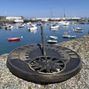 Garden Sundial Le Soliel Bronze Sculpture Anniversary Ornament AR002 angled side view of bronze sundial with Roman numeral dial overlooking marina and blue water
