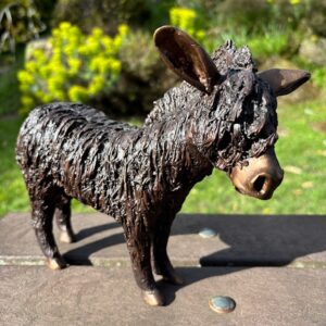 Bronze woolly donkey sculpture with textured coat standing outdoors in garden setting
