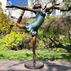 Elegant bronze ballerina sculpture posed gracefully in a garden setting