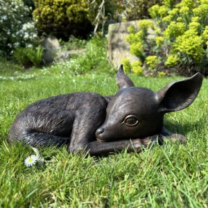 Bronze sleeping deer fawn sculpture resting in spring grass with daisies