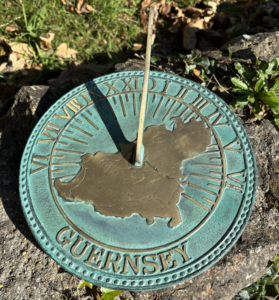 NEW Guernsey Sundial Solid Bronze Verdigris With Roman Numerals AR 20 positioned amongst natural rock formations with wild coastal flowers and verdigris patina.