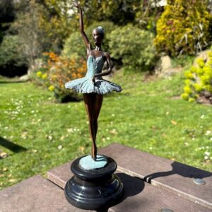 Elegant bronze ballerina sculpture with raised arm poised outdoors in garden setting