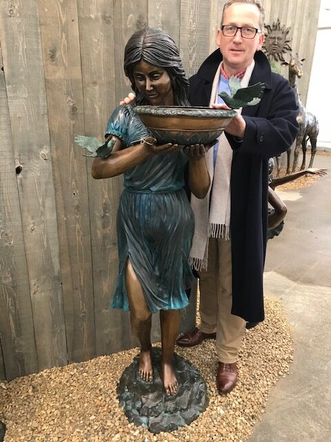 Bronze fountain sculpture of woman holding bowl with birds in garden setting