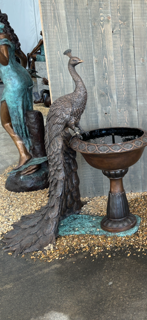 Bronze peacock fountain sculpture standing on pedestal bowl with flowing water feature in estate garden
