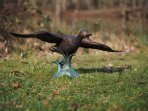 Bronze Flying Duck Water Feature Sculpture BI 105 low gliding pose on lawn with wings fully extended and natural outdoor setting