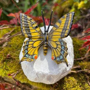 Bronze swallowtail butterfly sculpture mid flight on stone base with detailed patterned wings in a garden setting