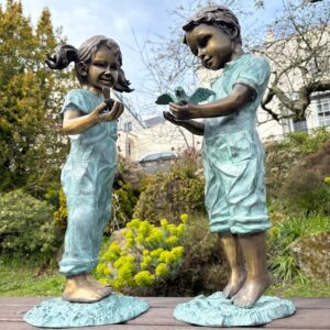 Bronze boy and girl with birds sculpture pair in garden setting