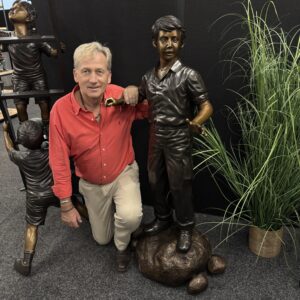 Bronze Young Boy Explorer Garden Sculpture FIBO 73 life-size bronze figure standing on textured rocks, photographed indoors beside ornamental grasses for scale and detail