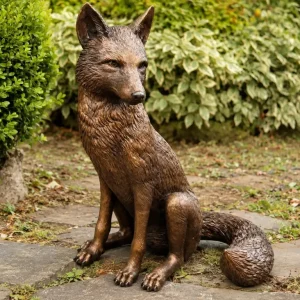 Sitting Fox Bronze Garden Sculpture with detailed fur, alert expression and sweeping tail, displayed naturally amongst garden greenery.