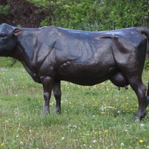 The Dairy Queen Lifesize Bronze Dairy Cow Sculpture MI 138 standing in a countryside meadow